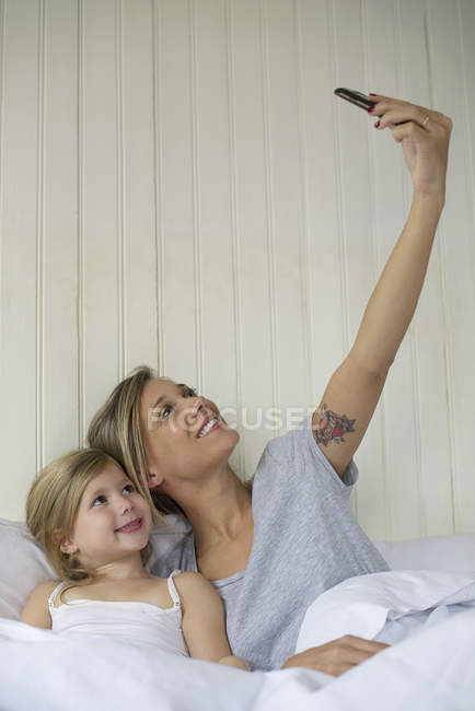 Мать и дочь позируют для селфи в постели — стоковое фото