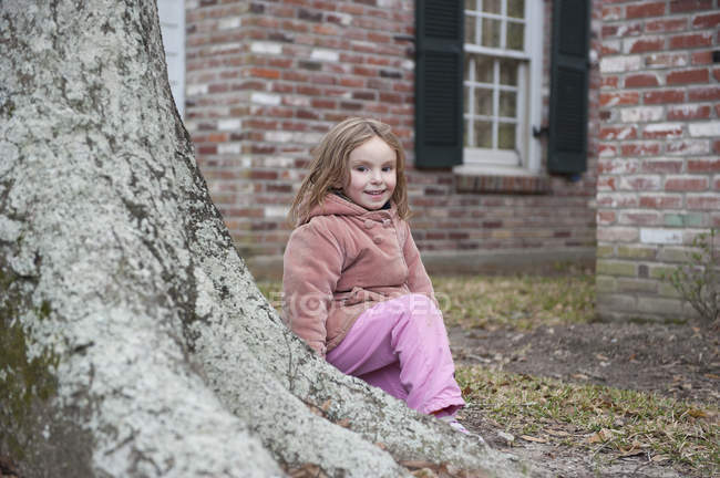 Little girl sitting at base of tree, smiling, portrait — Stock Photo