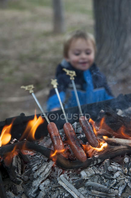Hotdogs cooking on grill at campground with boy on the background — Stock Photo
