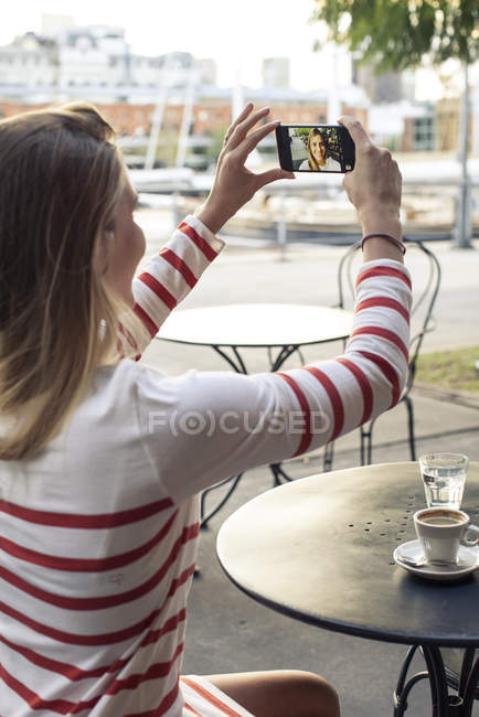 Молодая женщина делает селфи в кафе на тротуаре — стоковое фото
