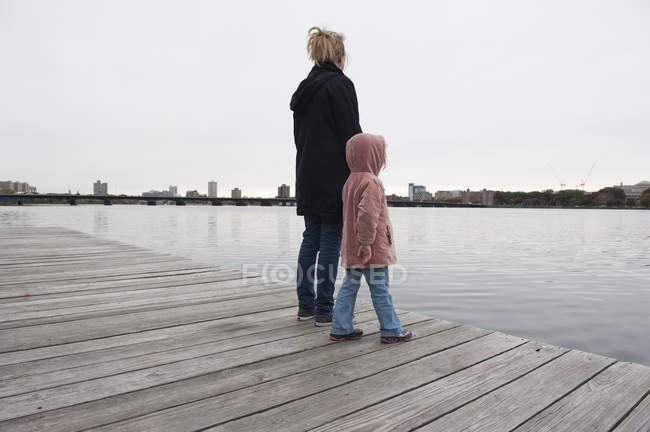 Mother and young daughter standing together on dock, looking at water — Stock Photo