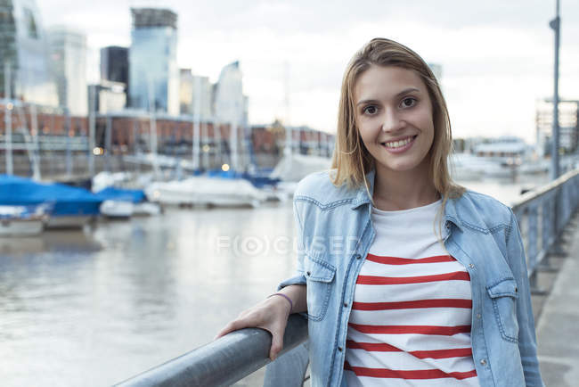 Mujer joven apoyada en barandilla y sonriente, retrato - foto de stock