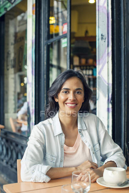 Mujer sonriente sentada en el café de la acera - foto de stock