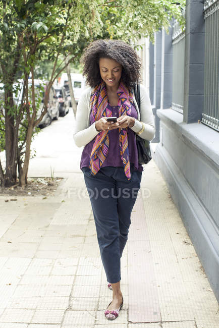 Woman texting message while walking on sidewalk — Stock Photo