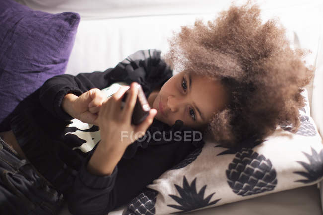 Fille couchée sur le canapé en utilisant smartphone — Photo de stock