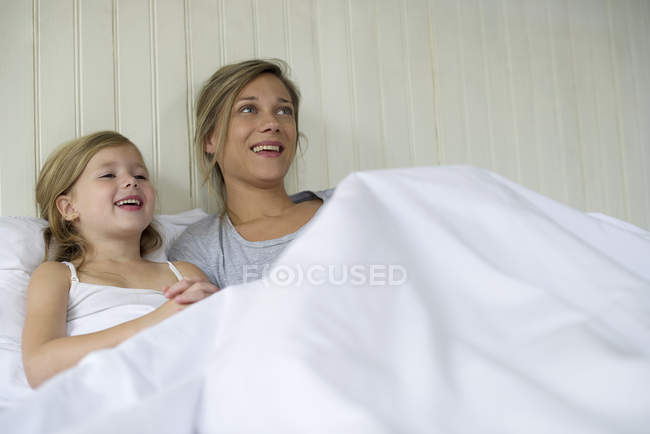 Madre e hija viendo televisión juntas en la cama - foto de stock