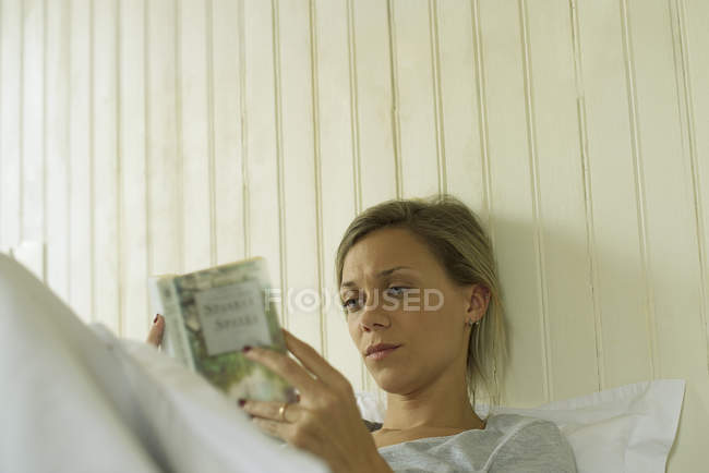 Giovane donna che legge a letto — Foto stock