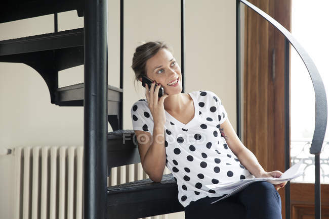 Женщина берет мобильный телефон, сидя на лестнице — стоковое фото