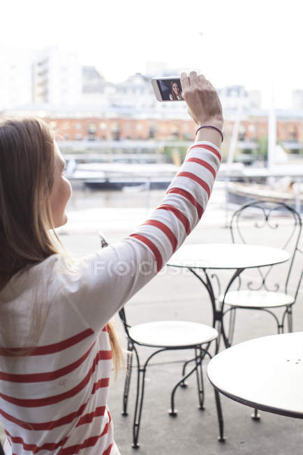 Молода жінка позує за селфі в тротуарному кафе — стокове фото