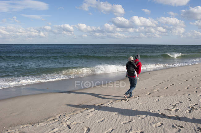 Urlauber spazieren am Strand mit kleinem Kind auf dem Rücken in der Nebensaison — Stockfoto
