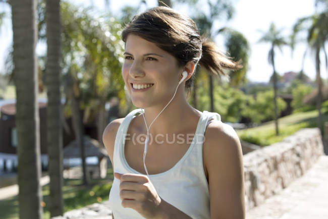 Mujer escuchando música mientras trota al aire libre - foto de stock