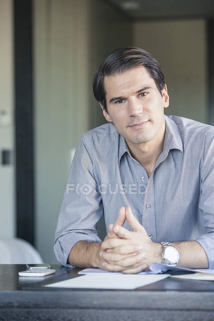Portrait of Businessman sitting at desk with clasped hands, — Stock Photo