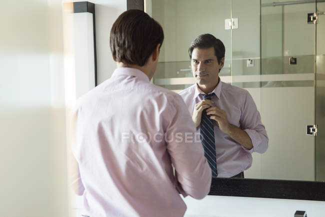 Чоловік дивиться у дзеркало у ванній кімнаті, регулюючи краватку — стокове фото