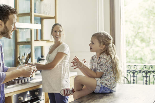 Chica charlando con los padres preparando comida familiar en la cocina - foto de stock