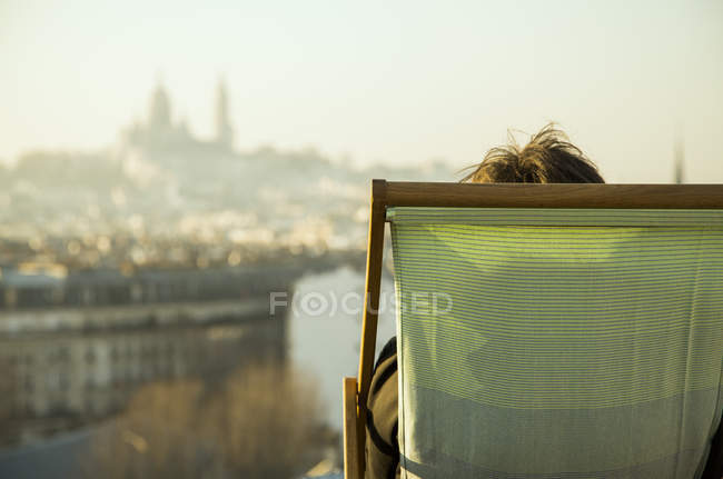 Persona seduta sulla sedia a sdraio, guardando la vista della città — Foto stock