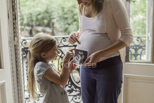 Mère utilisant une photo échographique pour préparer sa fille à l'arrivée imminente d'un nouveau frère et sœur — Photo de stock