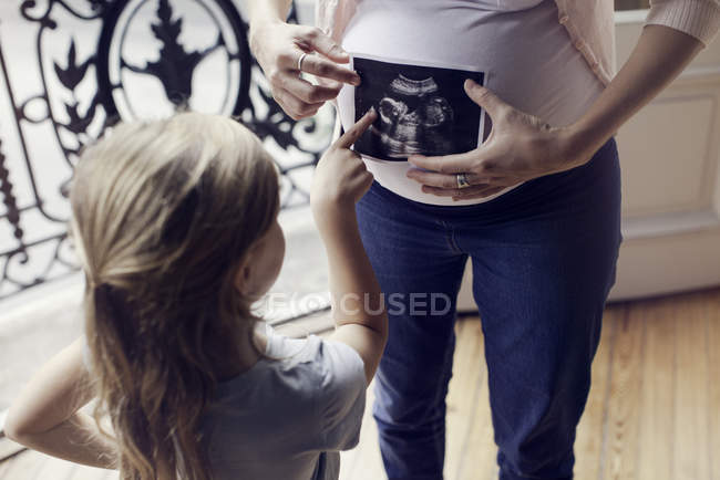 Madre utilizzando la foto ad ultrasuoni per preparare la figlia per l'arrivo imminente di nuovo fratello — Foto stock