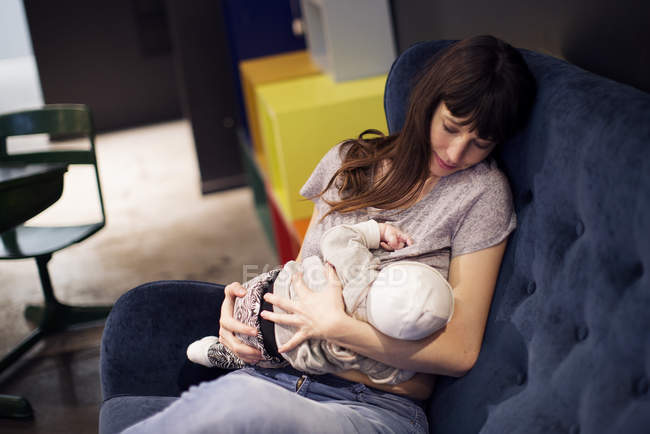 Мать кормящая младенца, сидящего на диване — стоковое фото
