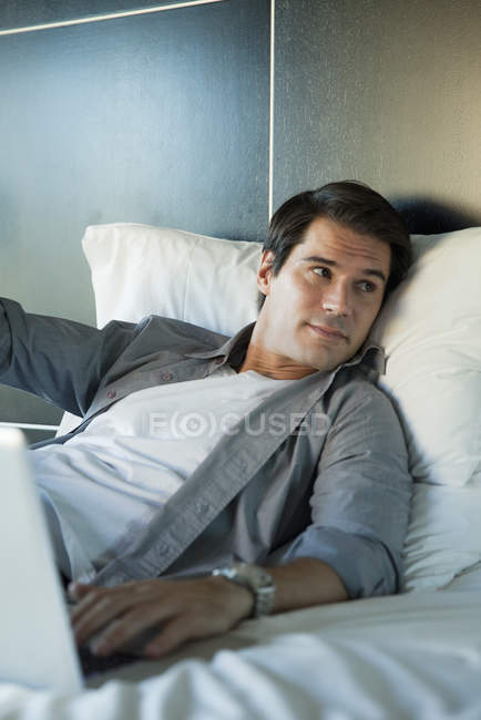 Homem relaxante na cama com computador portátil — Fotografia de Stock