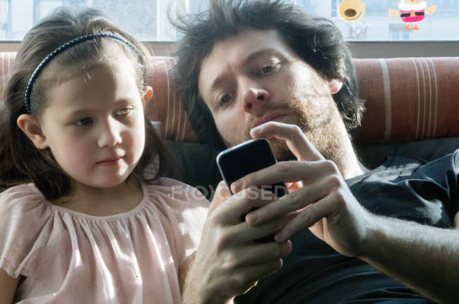 Отец и маленькая дочь вместе смотрят на смартфон — стоковое фото