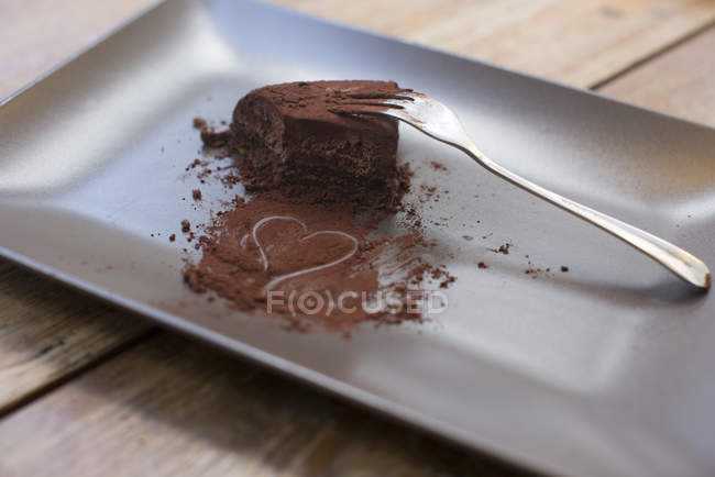 Herz in Kakaopulver gezogen und halb gegessen Schokoladenkuchen auf dem Teller mit Gabel — Stockfoto