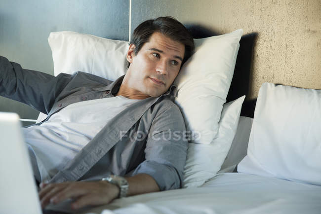Мужчина отдыхает в постели с ноутбуком — стоковое фото