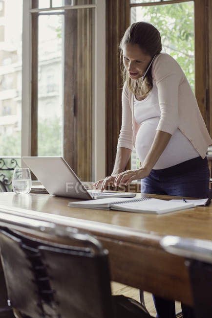 Беременная женщина работает из дома разговаривает по смартфону — стоковое фото