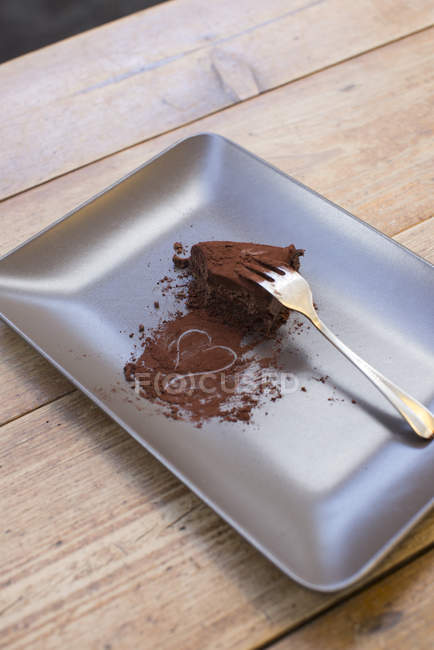 Corazón dibujado en polvo de cacao y pastel de chocolate medio comido en el plato con tenedor - foto de stock