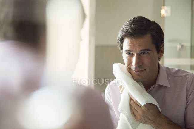 Mann schaut in Spiegel und trocknet sein Gesicht mit einem Handtuch — Stockfoto