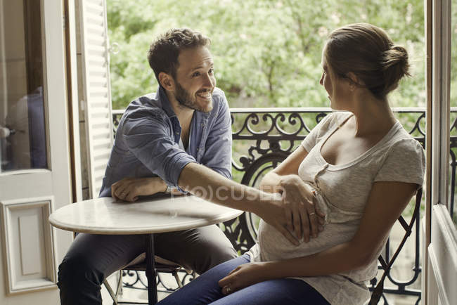 Marido sosteniendo el vientre de la esposa embarazada sentada a la mesa - foto de stock