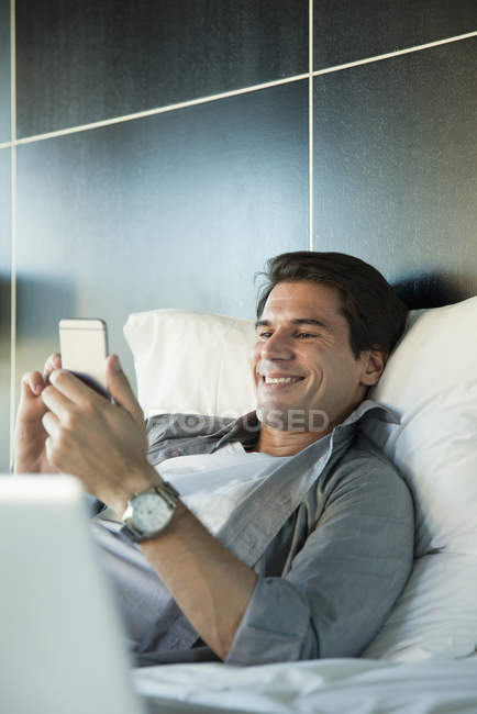 Homme relaxant au lit avec smartphone multimédia — Photo de stock