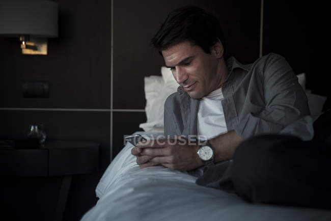 Людина розслабляється на ліжку з мультимедійним смартфоном — стокове фото