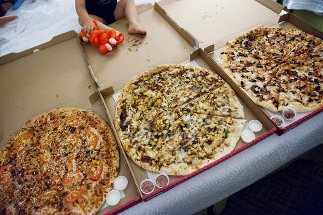 Criança sentada perto de pizza grande em caixas abertas — Fotografia de Stock
