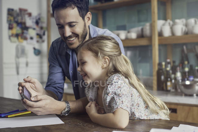 Батько і дочка дивляться на смартфон разом — стокове фото