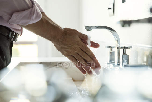 Обрезанное фото человека, моющего руки в раковине ванной комнаты — стоковое фото