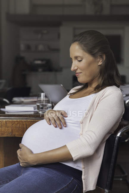 Retrato de la mujer embarazada acunando el vientre en casa - foto de stock