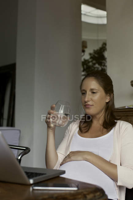 Mujer embarazada sosteniendo un vaso de agua de la casa - foto de stock