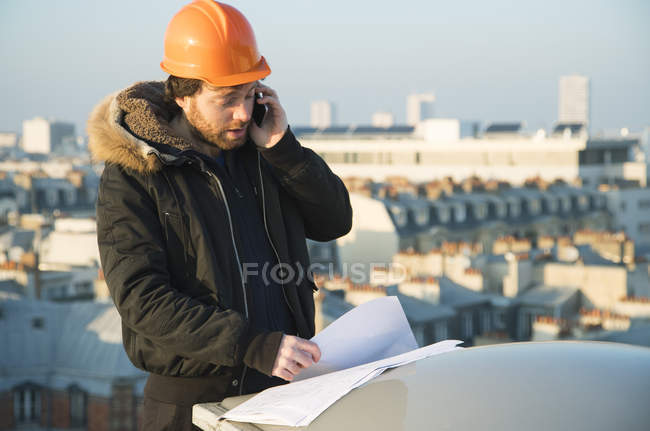 Construction supervisor studying blueprints and talking on cell phone — Stock Photo