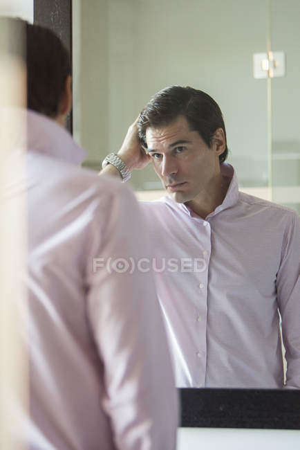 Uomo che si fissa i capelli allo specchio — Foto stock