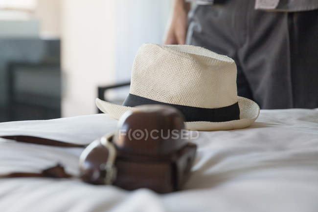 Camera and straw hat on bed in hotel room — Stock Photo