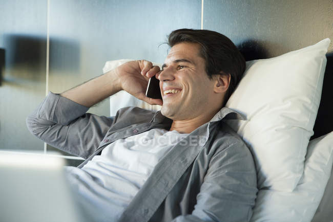 Усміхнений чоловік говорить на мобільному телефоні, лежачи в ліжку — стокове фото
