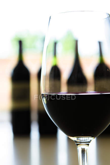 Закрыть бокал красного вина и бутылки вина на заднем плане — стоковое фото