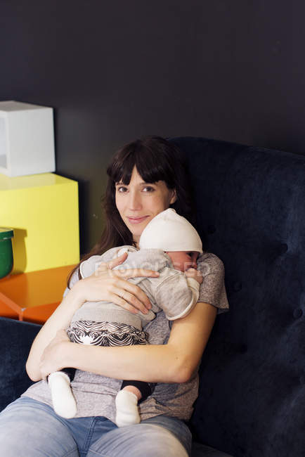 Мати тримає сплячого немовляти, сидячи на дивані — стокове фото