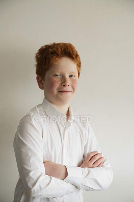 Портрет мальчика, уверенно улыбающегося со сложенными руками на сером фоне — стоковое фото