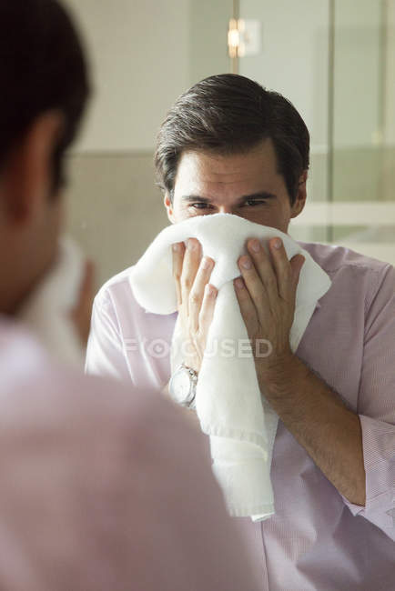 Чоловік дивиться у дзеркало, сушить обличчя рушником — стокове фото