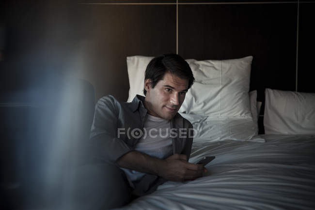Homem relaxante na cama com smartphone — Fotografia de Stock