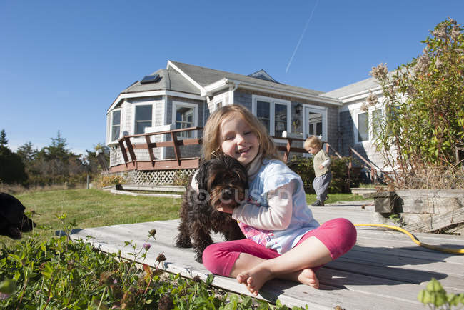 Little girl sitting on deck with dog — Stock Photo