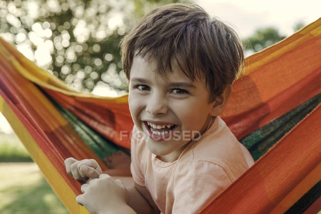 Портрет улыбающегося мальчика, сидящего в гамаке на открытом воздухе — стоковое фото