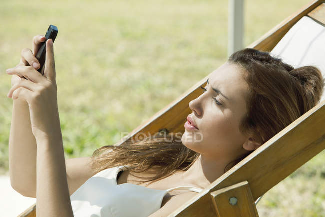 Молодая женщина смотрит на смартфон во время загорания — стоковое фото