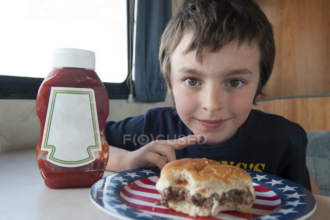Ritratto di ragazzo con hamburger sul piatto — Foto stock